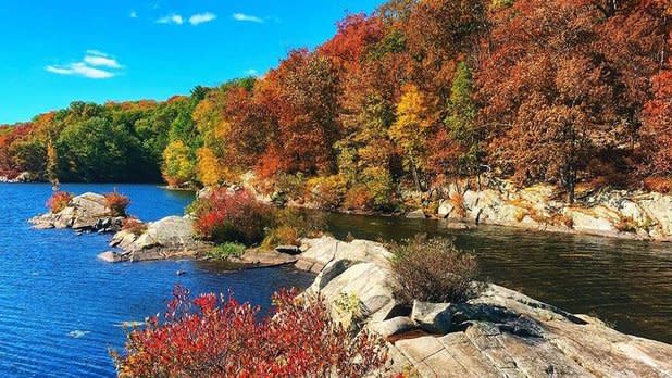View of orange and green foliage surrounding the lake at Fahnestock State Park