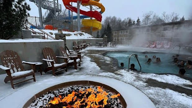 View from a snowy fire pit looking out at steaming hot springs and waterslide in winter