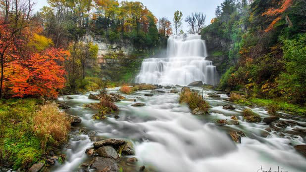 Water rushes down the falls surrounded by leaves changing from green to orange