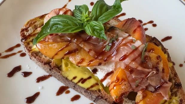 A slice of toast with avocado, smoked salmon, topped with basil with a vinaigrette drizzle at See & Be Kitchen.