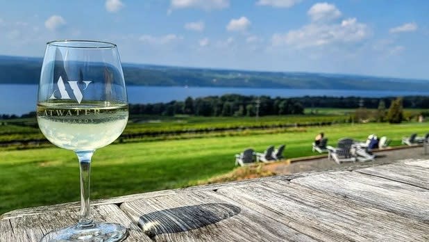 A glass of white wine from Atwater vineyards sits on a wooden table in front of a view of Seneca Lake