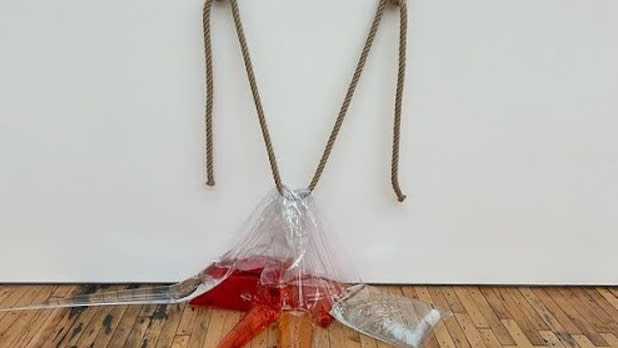 A rope holds up three clear plastic bags filled with red, orange, and clear liquid