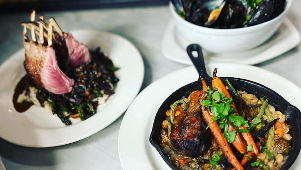 A skillet filled with orange carrots, meat, and other vegetables, a plat for ribs, and a bowl of black mussels
