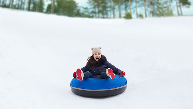 A girl with red shoes enjoys snow tubing on a blue and black donut down a snowy slope