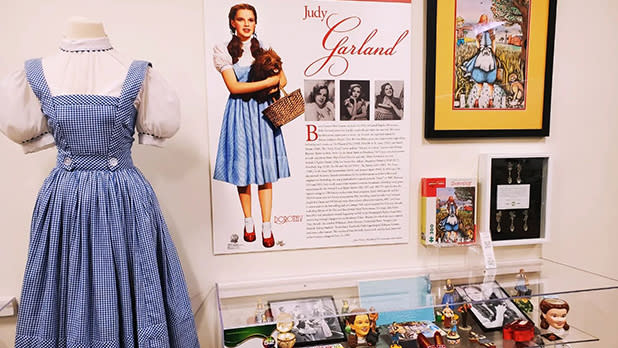 An exhibit of Judy Garland featuring images and a mannequin wearing Dorothy's blue dress on display at the All Things Oz Museum