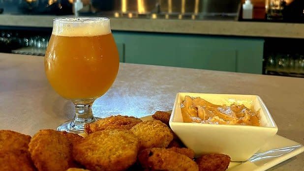 A beer and a plate of appetizers with sauce sit on the bar at Solitude Brewing