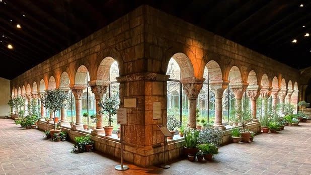 View from a corner of corridors lined with stone columns with a garden in the middle at the Met Cloisters