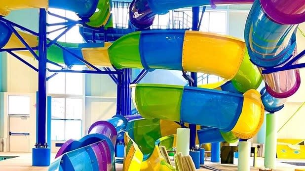 A colorful yellow, blue, green, and purple indoor water slide swirls around a pool below