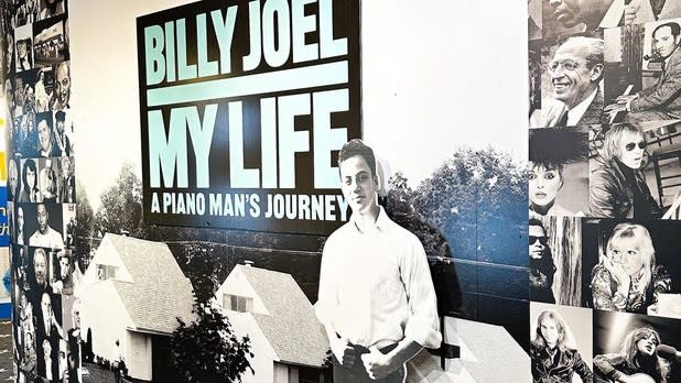 Display that says "Billy Joel- My Life, A piano Man's Journey" surrounded by photos and a cutout of young Billy Joel