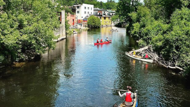 Various canoes and kayaks paddle through the waters of the Saranac River