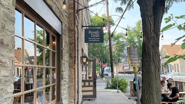 Street view of Rough Draft Bar & Books with people sitting to the right and the window looking into the shop to the left