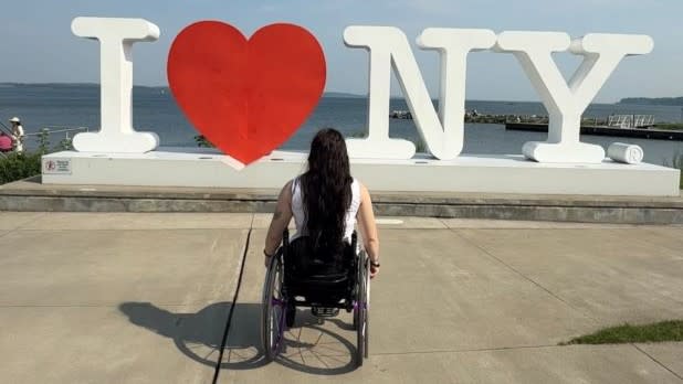 Tara Shetterly, who uses a wheelchair, looking at the "I LOVE NY" statue at the Finger Lakes Welcome Center