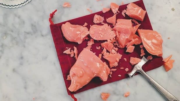 A pink peppermint pig candy on a red cloth that has been shattered by a small hammer