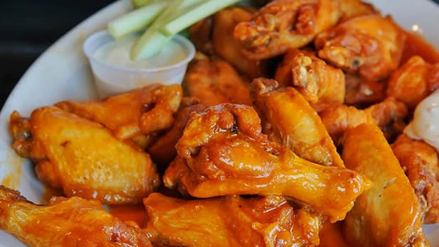 Chicken wings glistening in Buffalo sauce on a white plate with celery sticks and a cup of blue cheese dressing at Anchor Bar