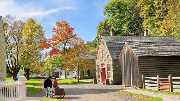 A man and a woman dressed in period clothes pull a wagon along a path at The Farmers' Museum on a fall day