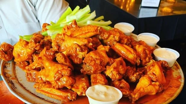 A plate full of buffalo wings with celery and cups of blue cheese