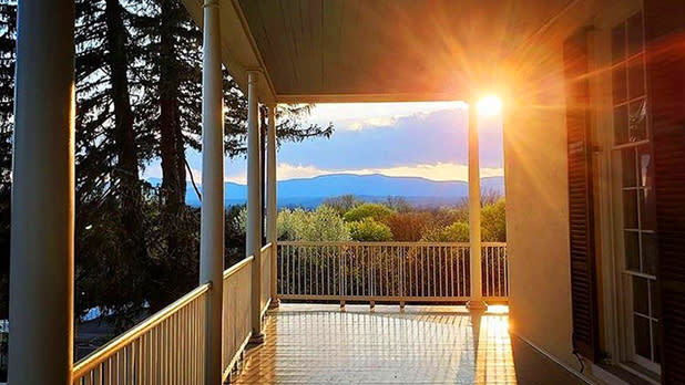 A view down the porch at Thomas Cole Historic Site with the tops of the trees in the distance and the sun setting in the upper right hand corner