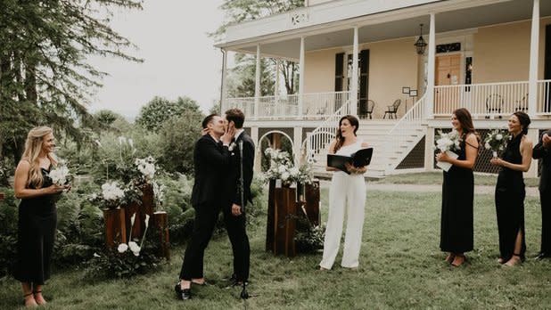 A couple shares a kiss surrounded by their wedding party on the lawn at the Thomas Cole Historic Site
