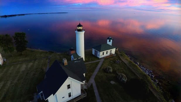 Aerial view of the white and black Tibbetts Point Lighthouse looking out to the water at sunset