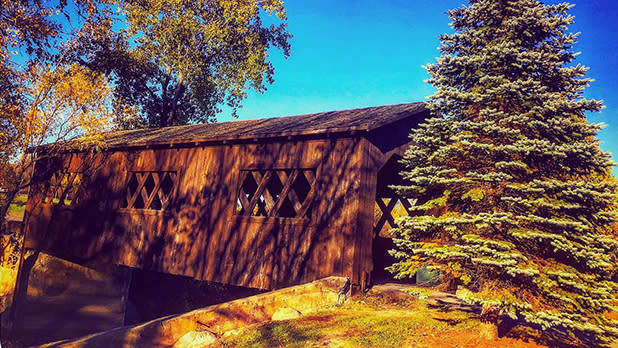 A quaint covered bridge in the Lake Champlain area of the Adirondacks, Ticonderoga’s Kissing Bridge stands amid trees in fall colors.