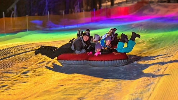 A family rides a tube down a lit up hill at Peek N Peak Resort