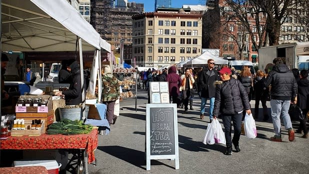 A woman carrying two shopping bags passes by vendors at the Union Square Greenmarket