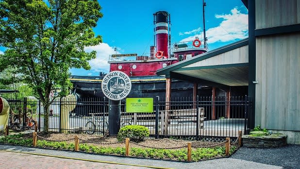 A red and black steam boat sits behind a sign for the Hudson River Maritime Museum