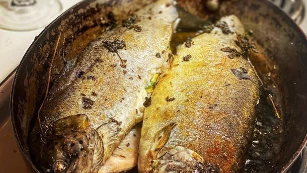 Two brown, green, and white trout being cooked in a pan