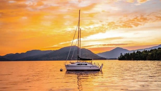 A sailboat on Lake George at sunset with mountains in the distance