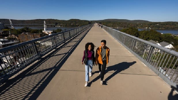 A couple walking across a paved elevated walkway on a sunny day