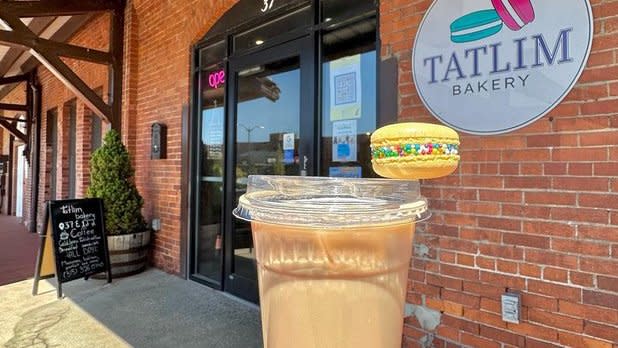 An iced coffee and sprinkle-covered macaron in front of the exterior of Tatlim Bakery