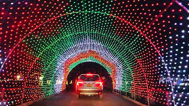 A white four-wheel drive car driving through a tunnel of red, green and white fairy lights at the Westchester Winter Wonderland Festival