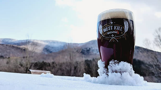 A pint of beer stands on a snow-covered table with mountains at the background at West Kill Brewing