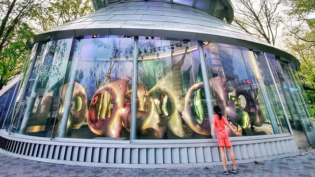 A girl looks at the iridescent glass fish figures that make up the SeaGlass Carousel in the Battery