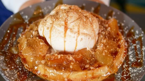 A golden waffle toppede with apple pie filling, vanilla ice cream, caramel, and powdered sugar