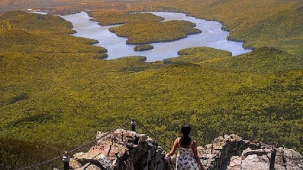 Woman in a white dress looking out at a body of water surrounded by green mountain tops