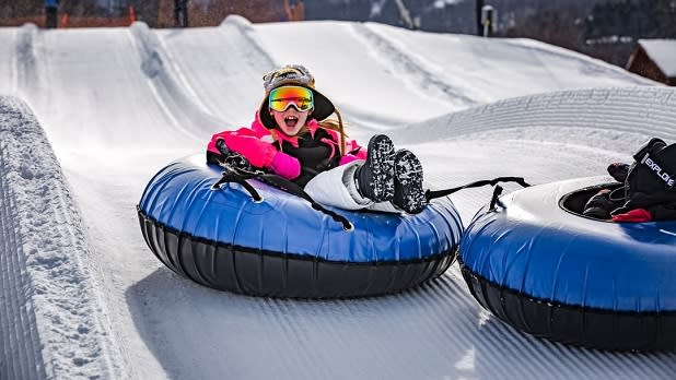 A smiling child slides down a hill in a blue tube at Windham Mountain