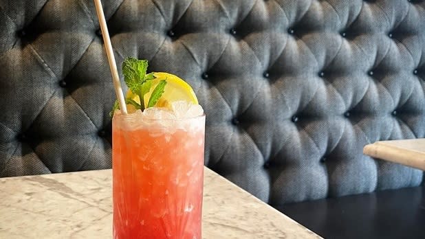 A dark pink/orange cocktail topped with green garnish and lemon at a booth table