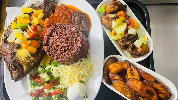 A plate with fried fish, fried plantains, jollof rice, beans, boiled egg, side salad, and noodles