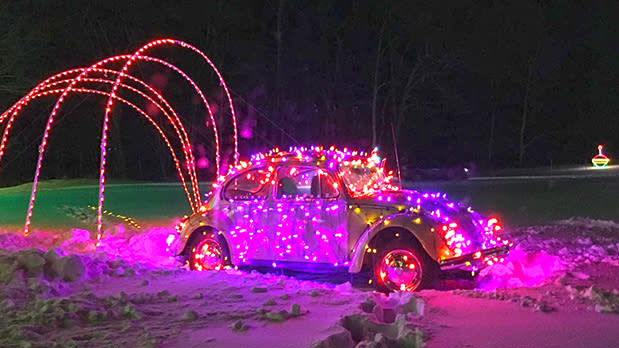 A yellow buggy vehicle completely covered in florescent pink fairy lights in front of multiple light arches in a snowy field