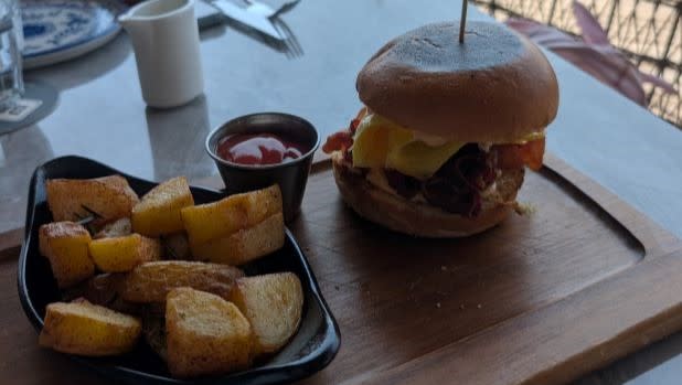 A cheeseburger slider and potato wedges with ketchup on a cutting board