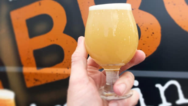 A person holds up a goblet-style glass filled with a hazy golden beer at Brickyard Brewing Co.