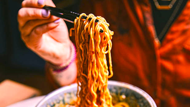 A close-up of a woman's pulling long life noodles from a bowl