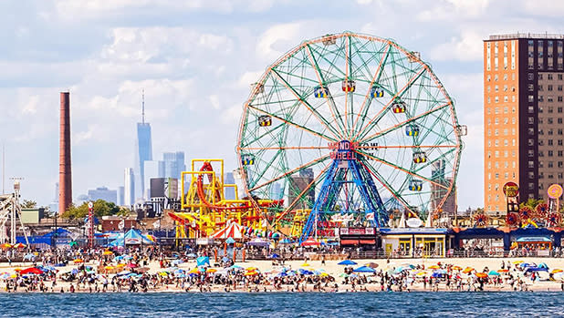 Crowds of beachgoers line the sand along the oceanfront at Coney Island with the Wonder Wheel towering in the background