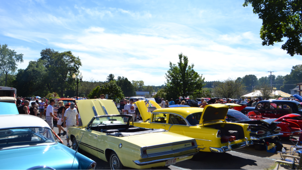 Sunny outdoor vintage car show with colorful classic cars, including a pale green convertible and bright yellow coupe, surrounded by crowds during the Adirondack Nationals Car Show in Lake George.