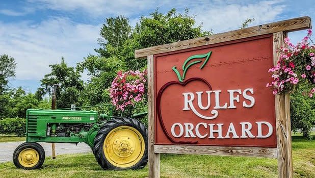 A green John Deere Tractor parked behind red sign that says "Rulf's Orchard"