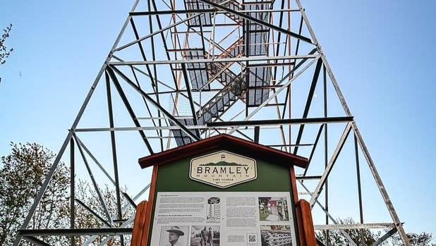 View looking up at the Bramley Mountain Fire Tower and a green sign that reads "Bramley Mountain Fire Tower" with historic information underneath