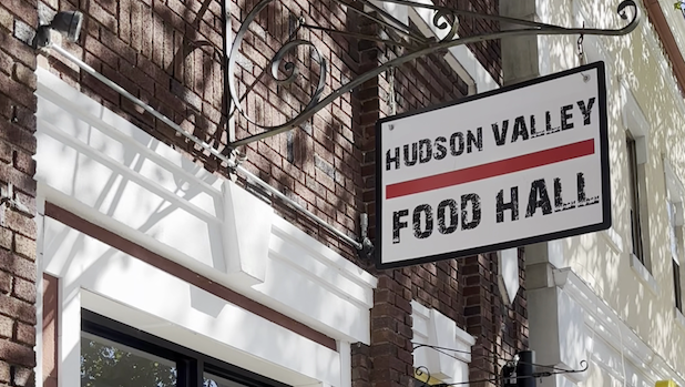 A white street sign that reads "Hudson Valley Food Hall" in black