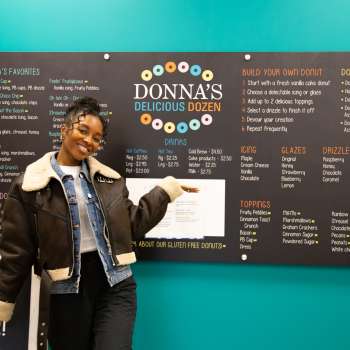 EC Contributor Jasmine Lawrence posing in front of Donna's Delicious Dozen sign