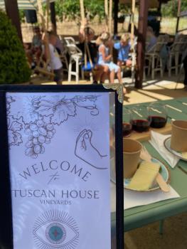Closeup of wine tasting menu art, with seated guests in the patio in the background at Tuscan House Vineyards